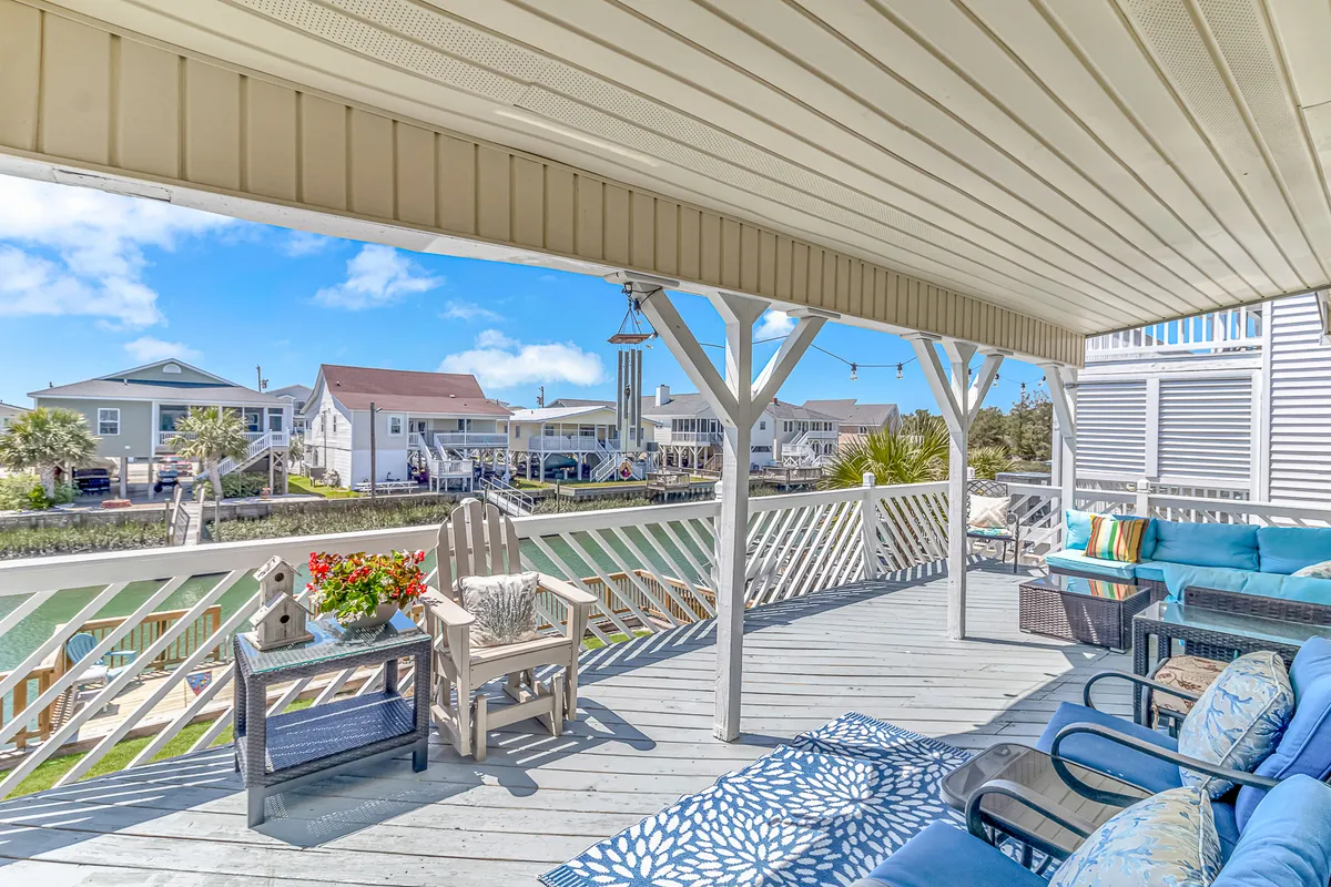 An inviting porch with a comfortable seating area, decorative rug, and flower planter overlooks the waterway, offering a tranquil spot to enjoy morning coffee and soft breezes.