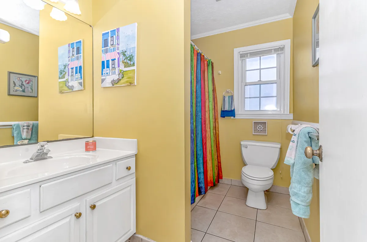 A vibrant bathroom showcasing a colorful shower curtain, a sleek vanity with a sink, and decorative wall art. The atmosphere feels inviting and fresh, reflecting comfort and convenience for guests.
