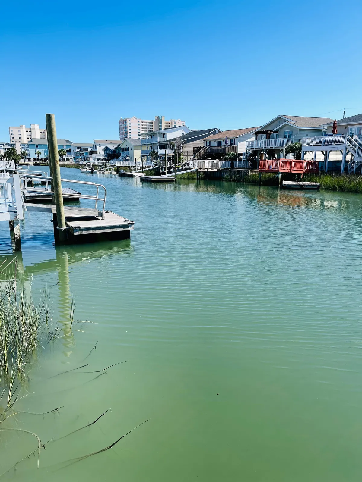 A tranquil channel view with boats gently floating by, a private dock in the foreground, and nearby houses lining the waterway. The image captures the essence of waterfront living, showing a space ideal for paddleboarding, fishing, or gathering with friends to watch the sunset.