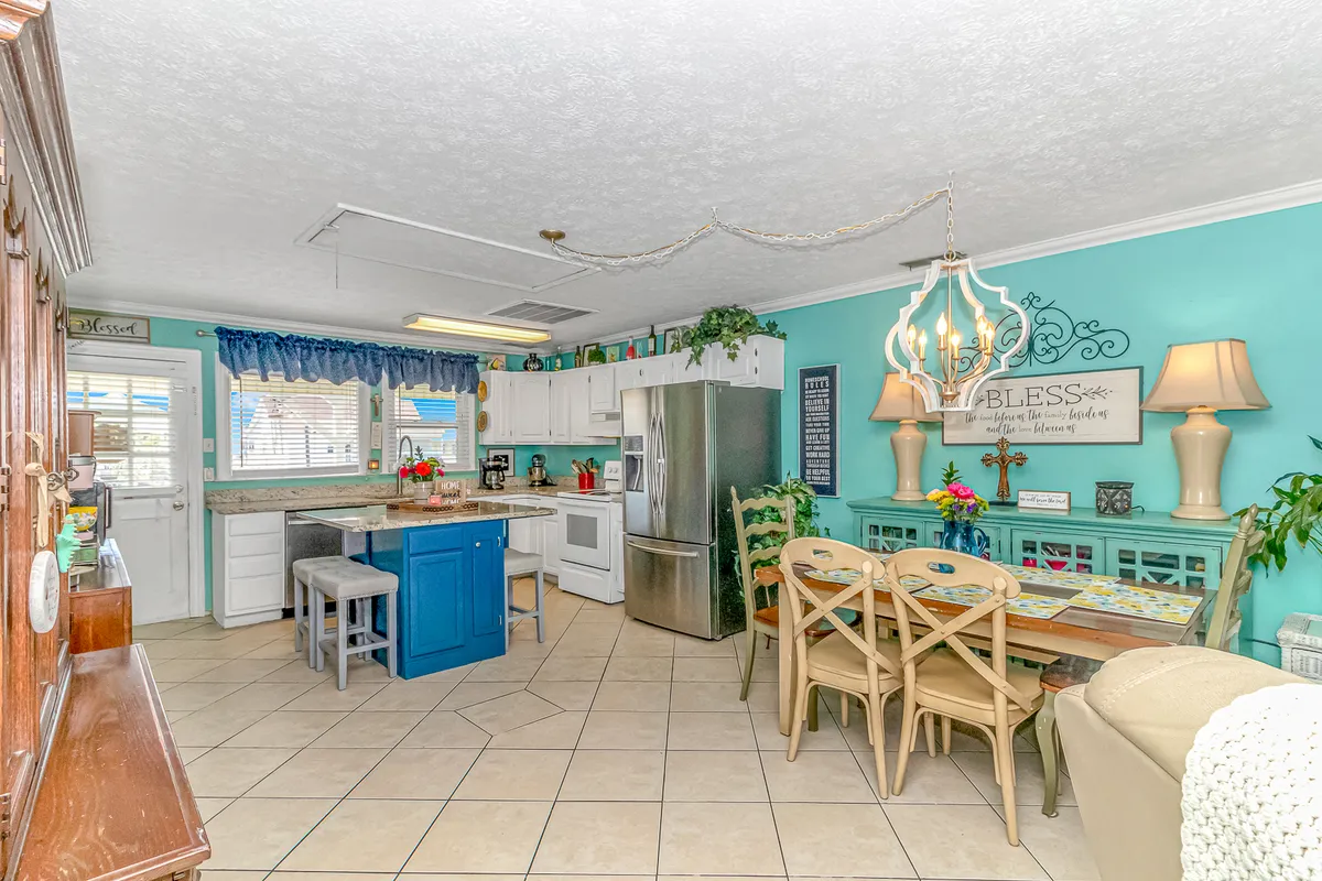 This photo shows a kitchen island, a dining table, a blue accent wall, decorative wall art, and stylish light fixtures. The layout highlights the flow between cooking and dining spaces, emphasizing a relaxed environment for casual meals and gatherings.