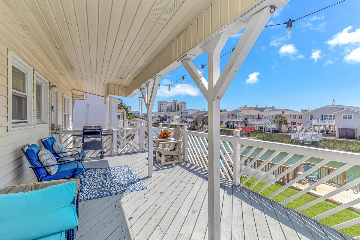 This exterior shot highlights a comfortable deck with a view of the waterway. The seating area is enhanced by a decorative blue rug and string lights overhead, creating an inviting atmosphere for outdoor meals and relaxation. The setting is perfect for watching boats pass or letting dogs splash in the water nearby.