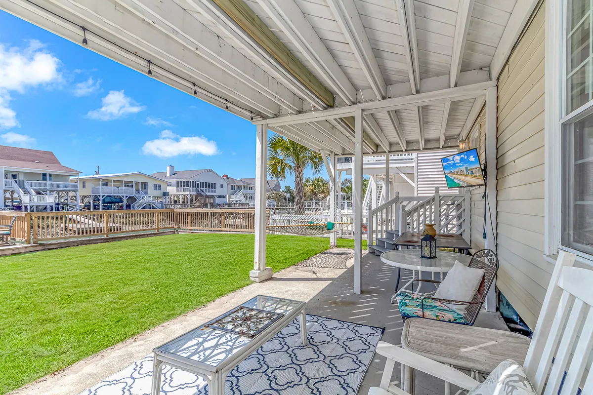 This image features a comfortable outdoor seating area set on a lush green lawn, surrounded by palm trees and adjacent homes. The space is inviting and open, well-suited for gatherings, relaxing in the shade, and enjoying the outdoors. The presence of a decorative outdoor table and ample space suggests it’s ideal for both people and pets to enjoy.