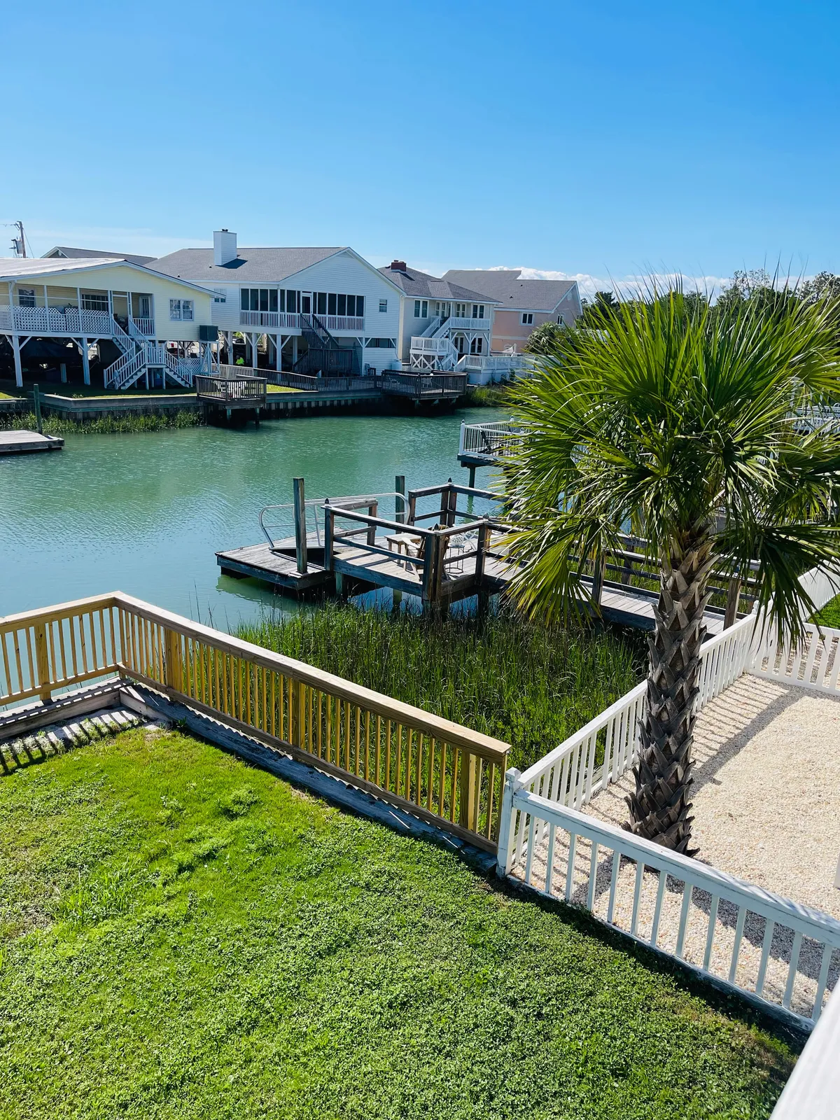 This image showcases a tranquil waterway bordered by a green lawn, palm tree, and private docks. The scene evokes the feeling of direct waterfront access and opportunities for water-based activities like boating and fishing, as well as relaxing by the water's edge.